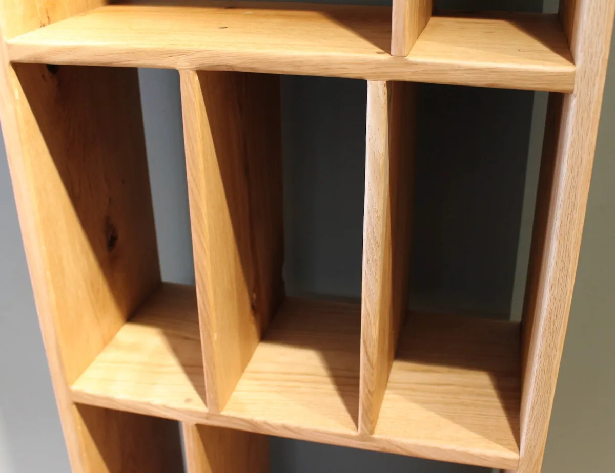 Firāq — solid oak shelving unit, uprights in raking light